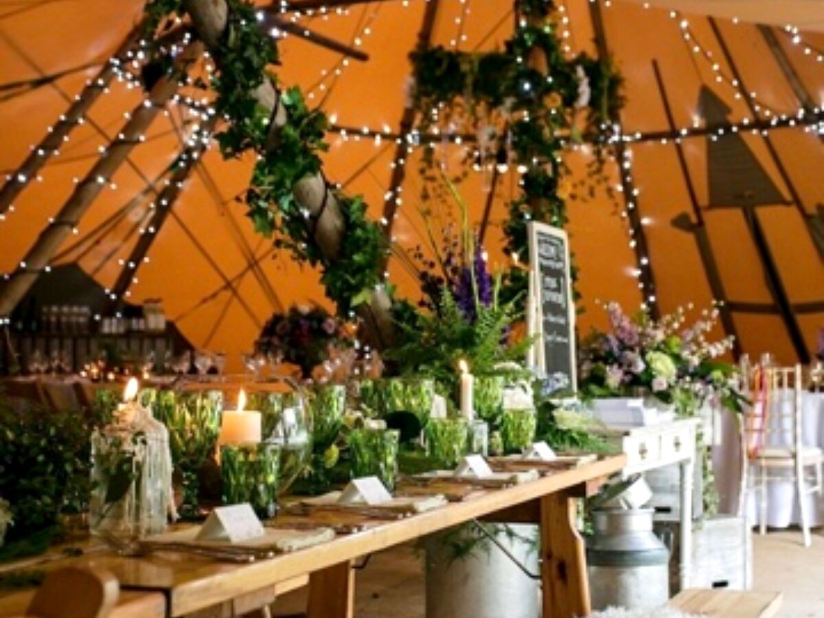 Rustic wedding tables dressed with greenery inside a softly lit tipi.