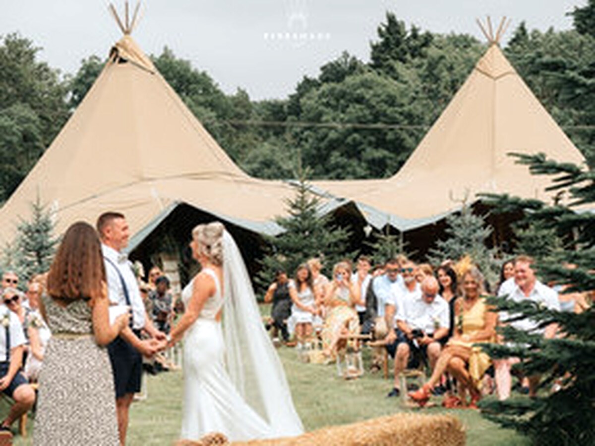 Bride and groom during an outdoor wedding ceremony beside linked tipis.