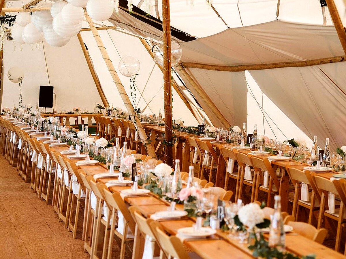 Long wooden wedding tables styled with flowers and lanterns inside a tipi.