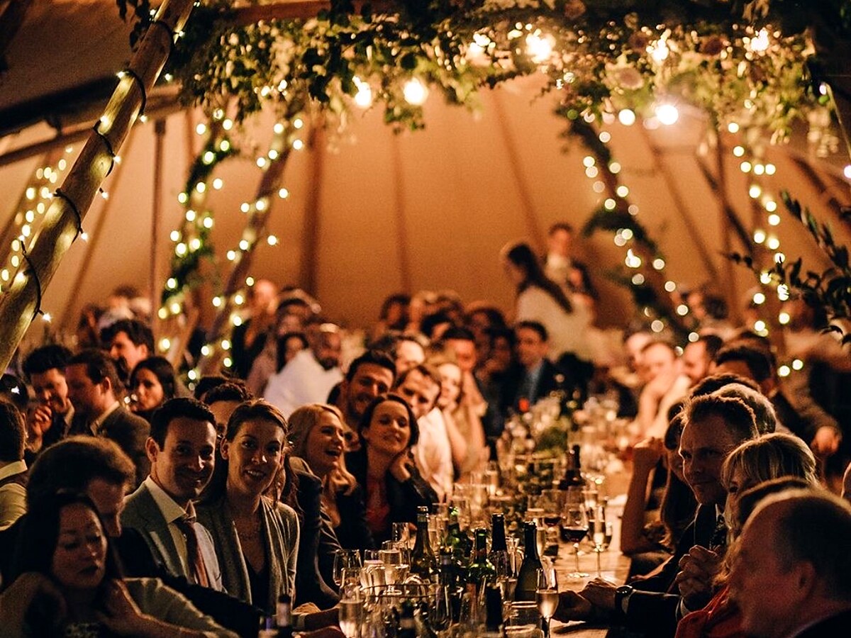 Wedding guests dining beneath greenery and fairy lights inside a tipi.