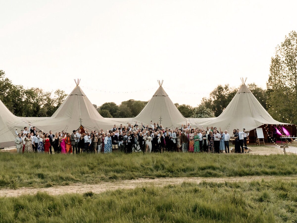 Wedding party gathered in front of linked tipis in a Yorkshire field.