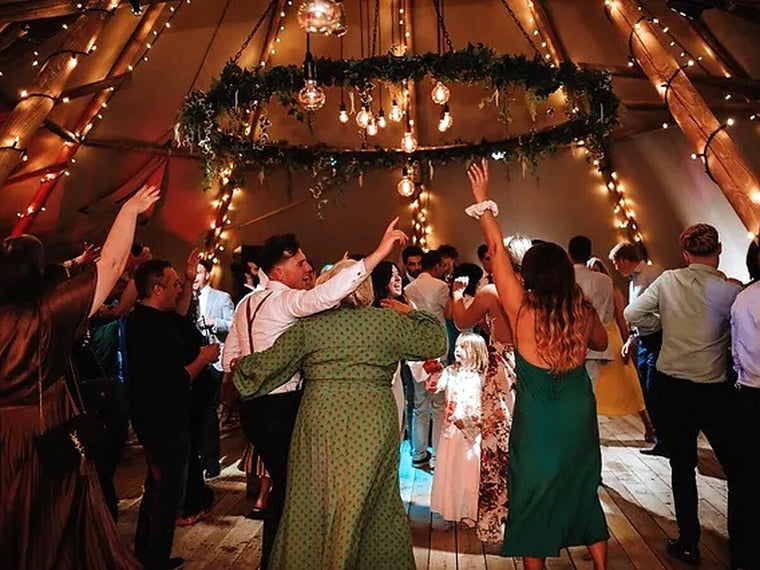 Wedding guests dancing beneath fairy lights inside a tipi.
