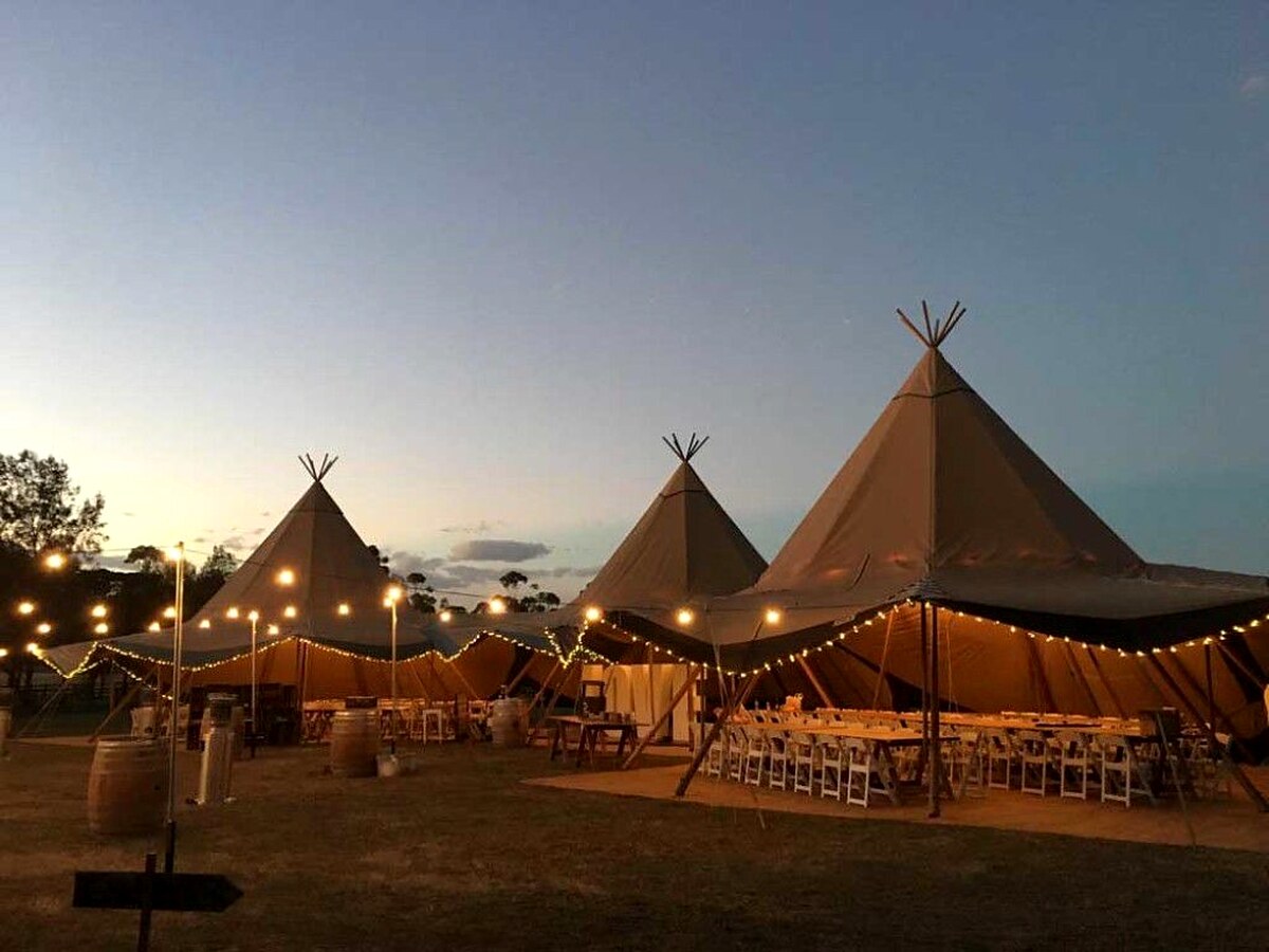 Connected wedding tipis glowing with festoon lights at dusk.