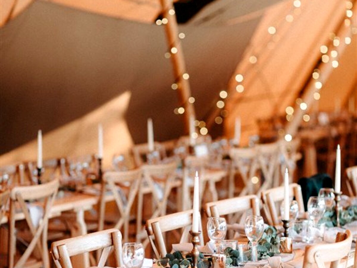 Warmly styled wedding tables beneath fairy lights inside a tipi.